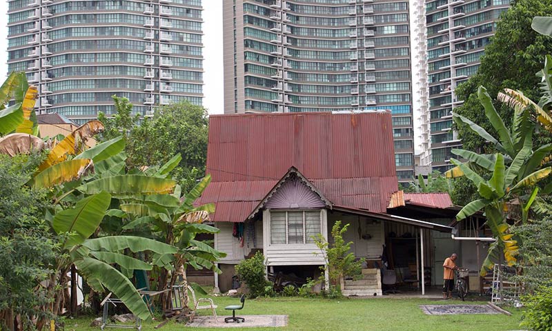 A traditional malay house in kampong bharu, overshadowed by high-rise apartment towers