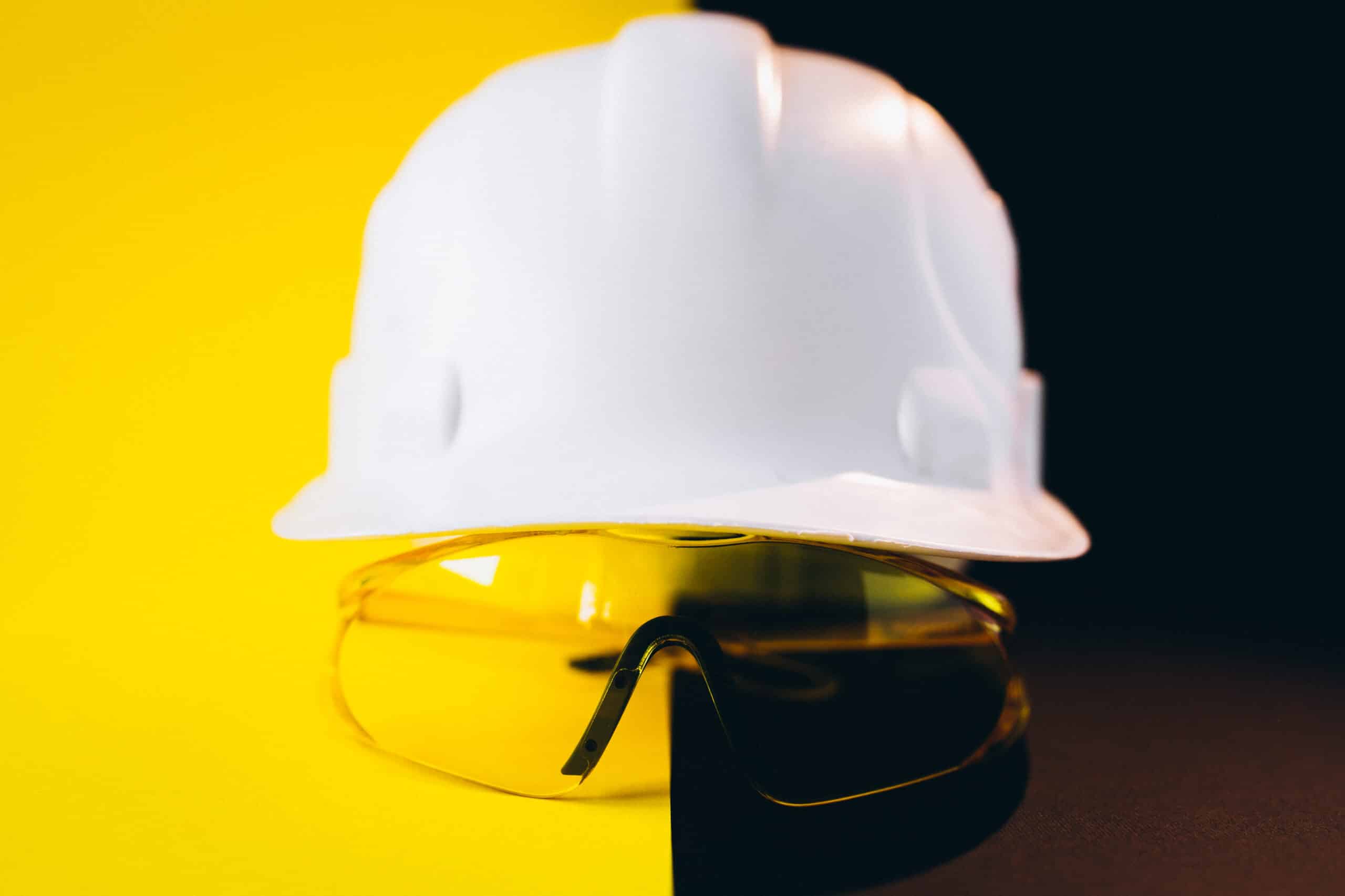 White hard hat with protection eyeglasses isolated on a black and yellow background