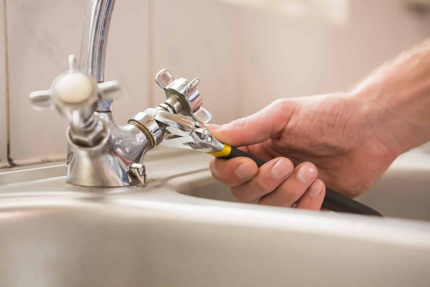 Man fixing tap with pliers at home in the kitchen