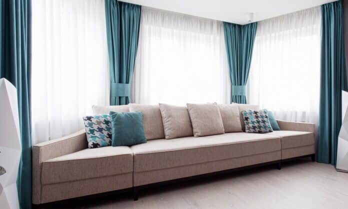 Large modern couch in the room near a big window, light and turquoise tones