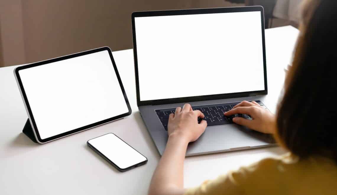 Yellow shirt woman using laptop and tablet, phone placed on the table, mock up of blank screen.