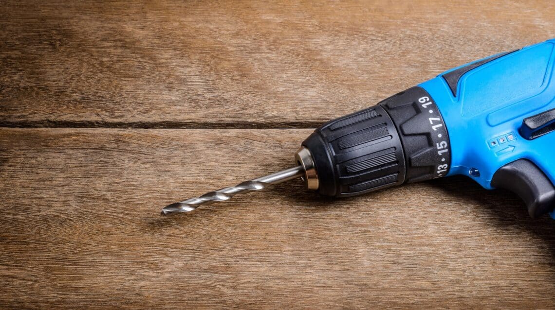 Close up electric drill on wooden table background and copy space. Hammer drill or screwdriver, electric cordless hand drill on wooden. Maintenance home concept.