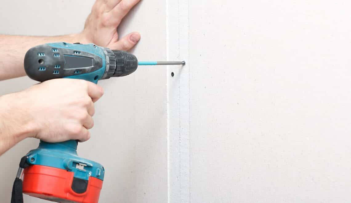 A man with a screwdriver in his hand fastens drywall to the wall