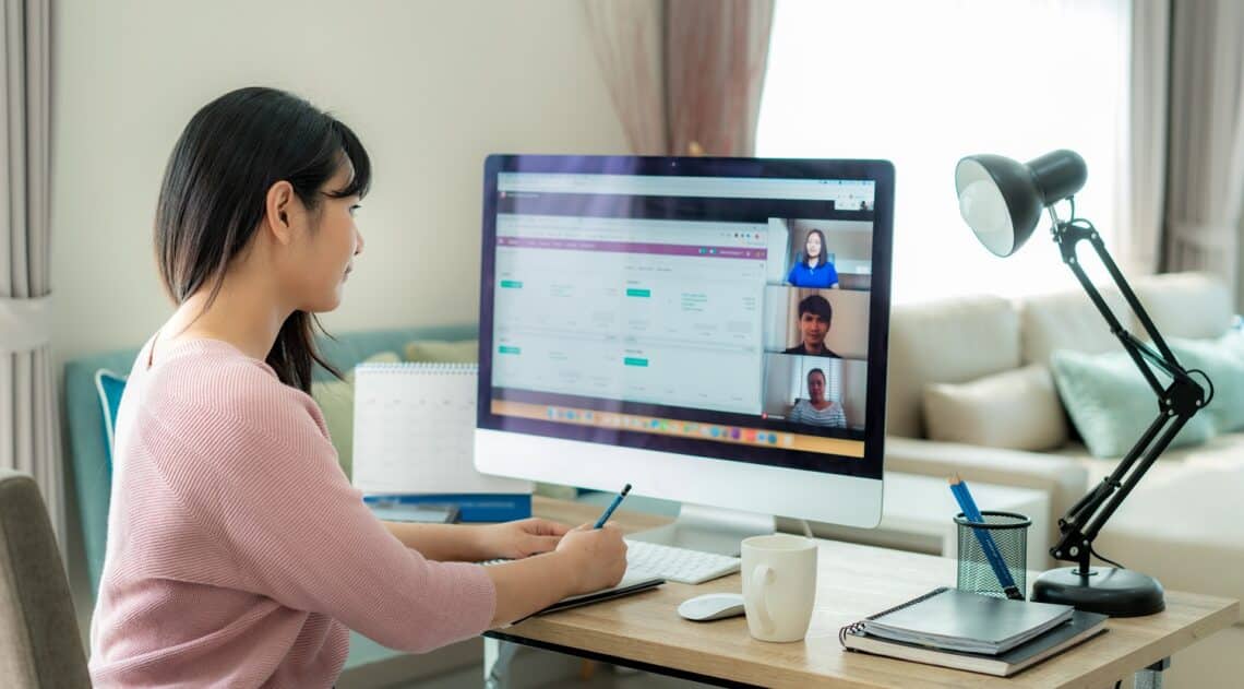 Back view of asian business woman talking to her colleagues about plan in video conference. Multiethnic business team using computer for a online meeting in video call. Group of people smart working from home.