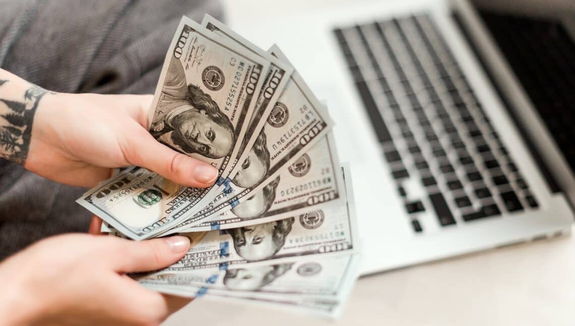 Freelance work concept - close up of woman hands holding new dollar bills she earned working from laptop at home online