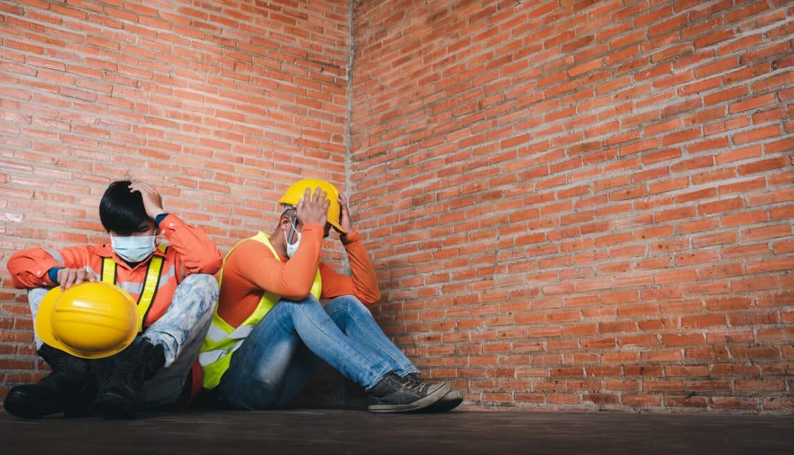 Two construction workers regret sitting sad at the job site wearing a medical mask to prevent covid-19 is unemployment and the economic crisis. Unemployment failed during covid-19