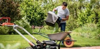 Gardener emptying lawn mower grass into a wheelbarrow after mowing. Landscape design. Gardening
