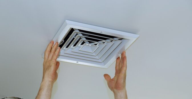 Close up man hand installing vent cover from ceiling mounted air conditioner.