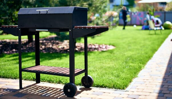 Barbecue grill on wheels with wooden stands in the garden. Tasty and wholesome food in the heat. Future shish kebab. For holidays and events