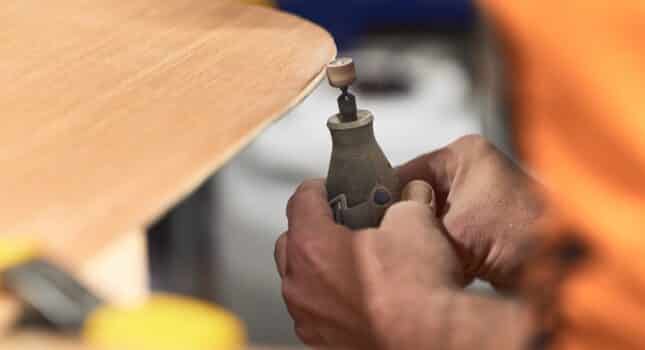 Detail of carpenter's hands filing the edge of a wooden plank with a dremel tool. Top view