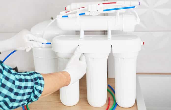 Installation purification osmosis system. Plumber or man hand replace water filter cartridges at home kitchen. Close up.