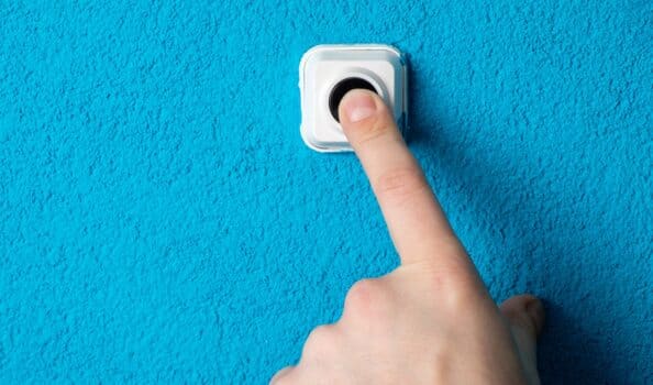 Close-up of man's hand pressing the button of doorbell on blue wall