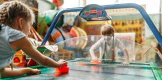 Two happy girls plays air hockey in children game center. Excited childs having fun on playground indoors. Kids playing on machine in amusement centre
