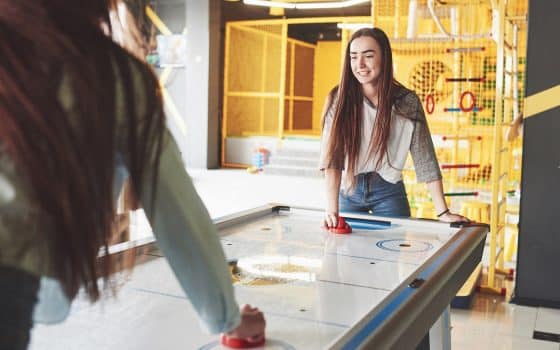 Two beautiful twin girls play air hockey in the game roomand have fun.