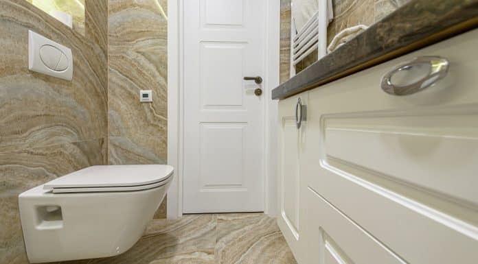 Spacous luxury bathroom with white water toilet, cabinet and beige marble tiles