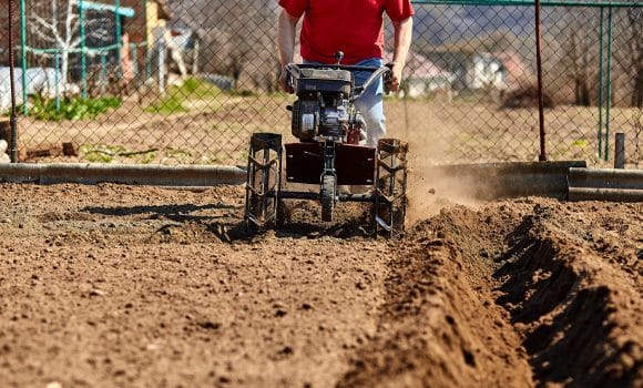 Gardener man cultivate ground soil with tiller tractor or rototiller, cutivator, miiling machine, prepare for planting crop in spring. Modern farming, technology agriculture.