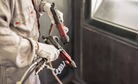 Paint shop worker with industrial sprayers in his hands, close-up