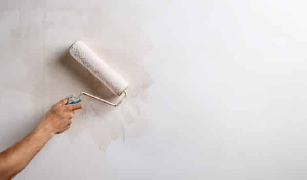 Close up photo of hand painting wall with roller in white color. Copy space.