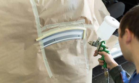 Close-up of a spray gun with white paint for painting a car in a special booth.