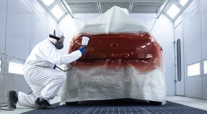Professional painter in protective clothing applying varnish layer and finishing painting of the car.