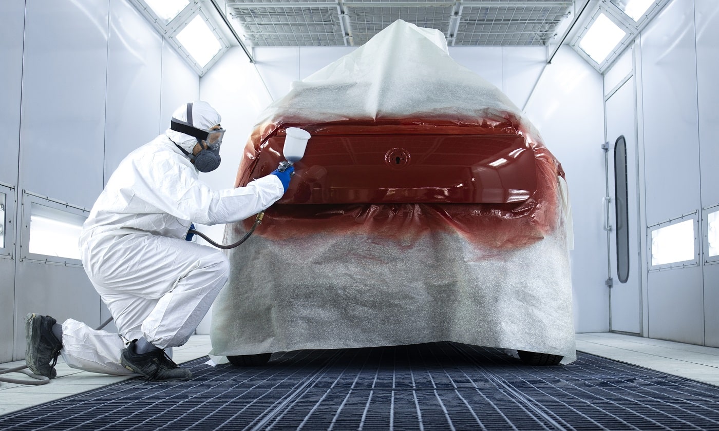 Professional painter in protective clothing applying varnish layer and finishing painting of the car.