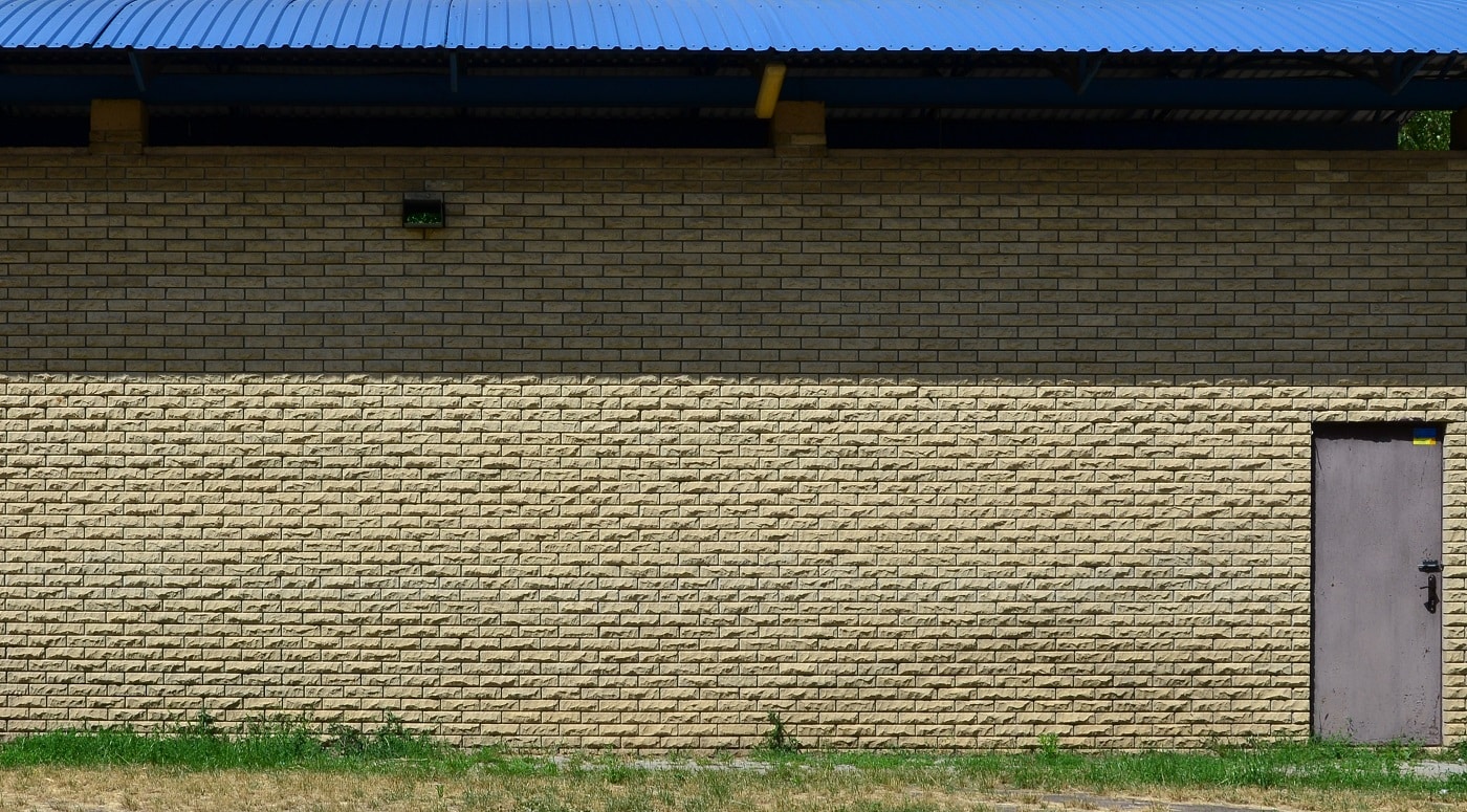 Texture of brick wall from relief stones under bright sunlight with two metal doors