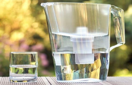 Plastic water filtration pitcher and a clean glass of a clear water on the summer garden background in sunny warm summer evening in countryside