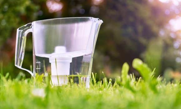 Water filter jug standing on the green grass in summer garden in warm morning. Water filtration concept.