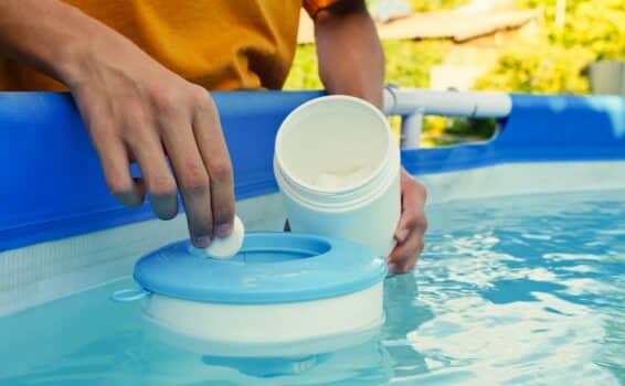 Hand holding white chlorine tablets over swimming pool skimmer. Chlorination of water in pool for disinfection and prevention against the development of microbes. High quality photo