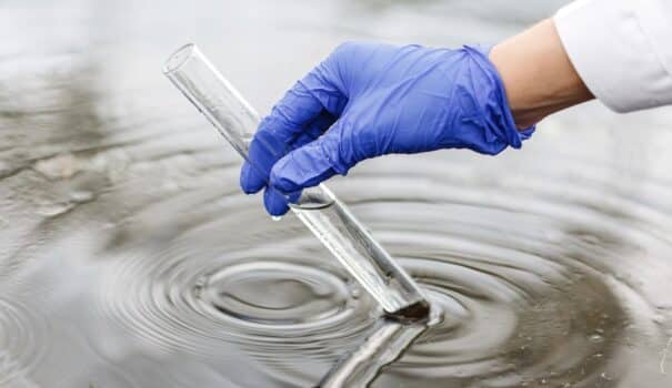 Researcher holds a test tube with water in a hand in blue glove