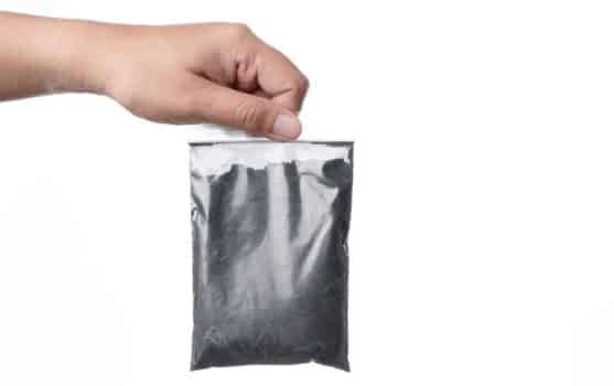 Hand holding plastic zipper bag of charcoal powder on white background