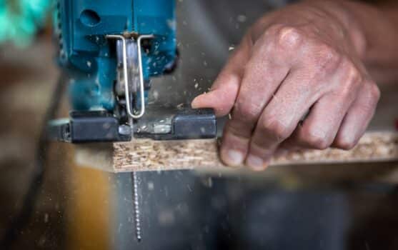 Close-up of a carpenter's hands in the process of cutting wood with a jigsaw.