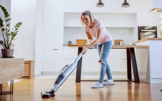 Smiling worthy caucasian blond housewife dressed casual using steamer to clean parquet in her apartment.