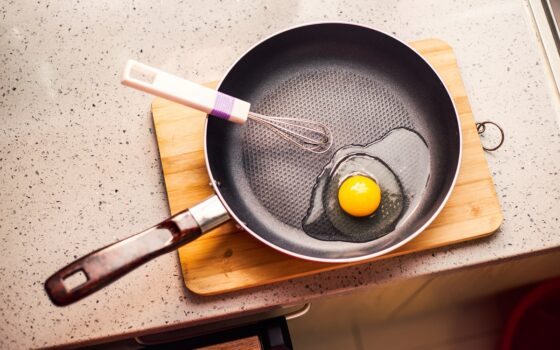 Fried egg in frying pan and whisk on wooden background good photo