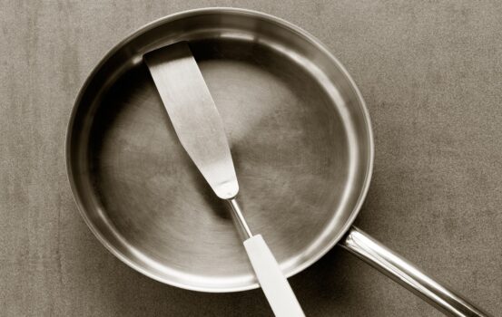 Used clean empty stainless steel frying pan and spatula overhead view on the gray background, black white photos. Closeup top view