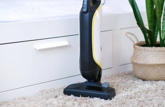 Cordless vacuum cleaner is used to clean the carpet in the room. Housework with a new handheld vacuum cleaner. House cleaning, care and technology concept.