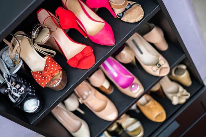 Gray wooden closet shelves full of fashion female shoes on heels pair closeup. Storage organization of cupboard row with stylish multicolored feminine footwear neatly folded. Shelf organizer cabinet