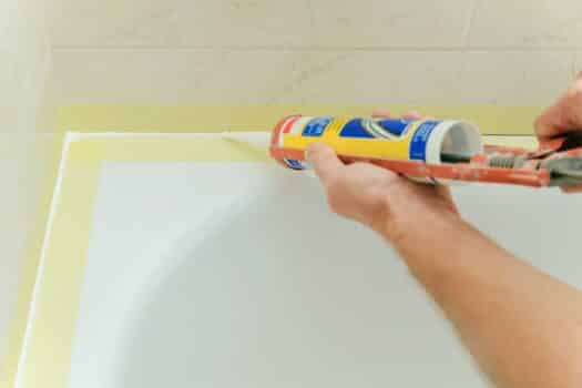 Worker puts silicone sealant to caulk the joint between tub and wall.