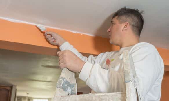 Young male painter using a brush to paint the details of a ceiling. Concept of specialized work, professional job.