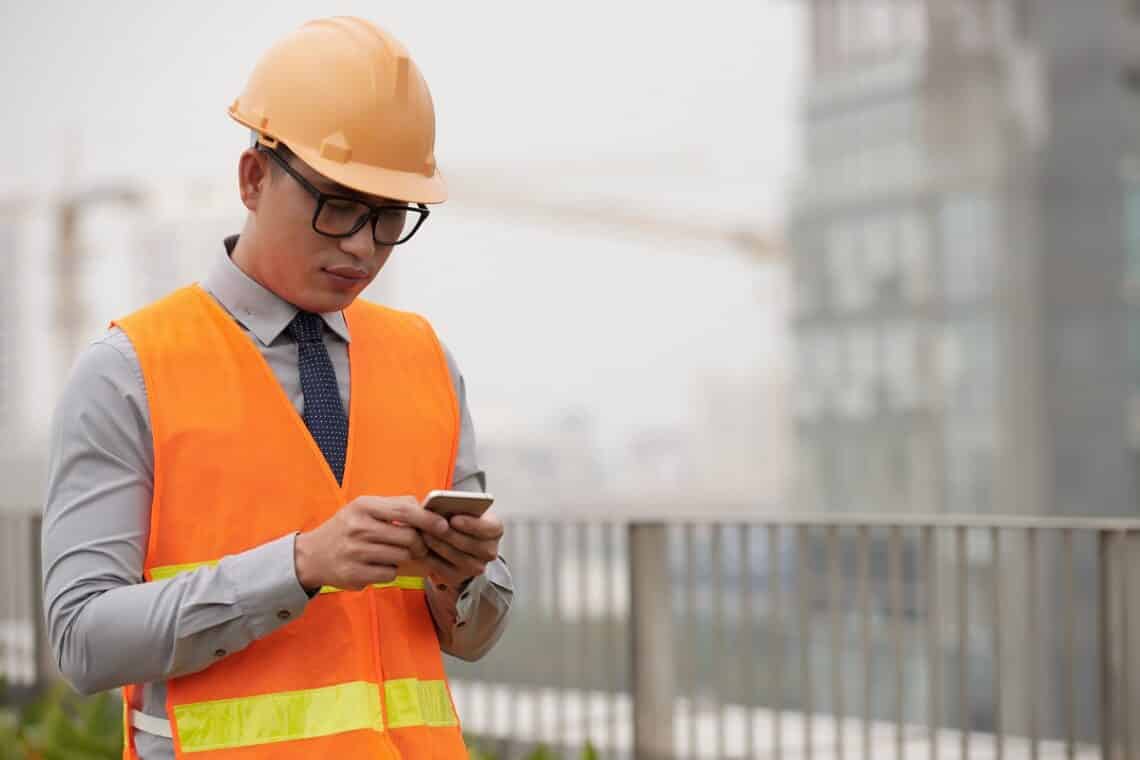 Construction site worker reading messages on the best apps for architects