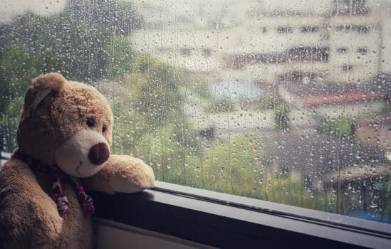 Brown teddy bear sitting beside the window while raining