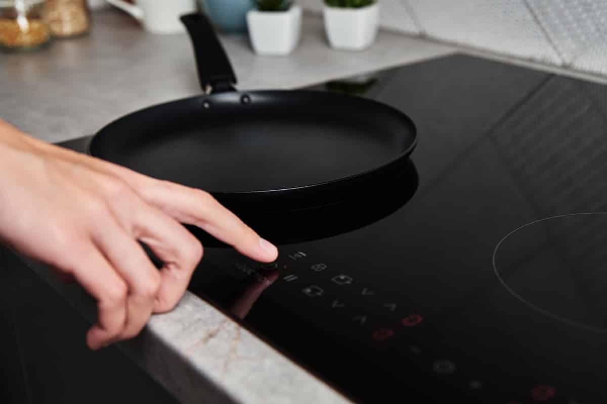 Modern kitchen appliance. Woman hand turn on induction stove to cook. Finger touching sensor button on induction or electrical hob
