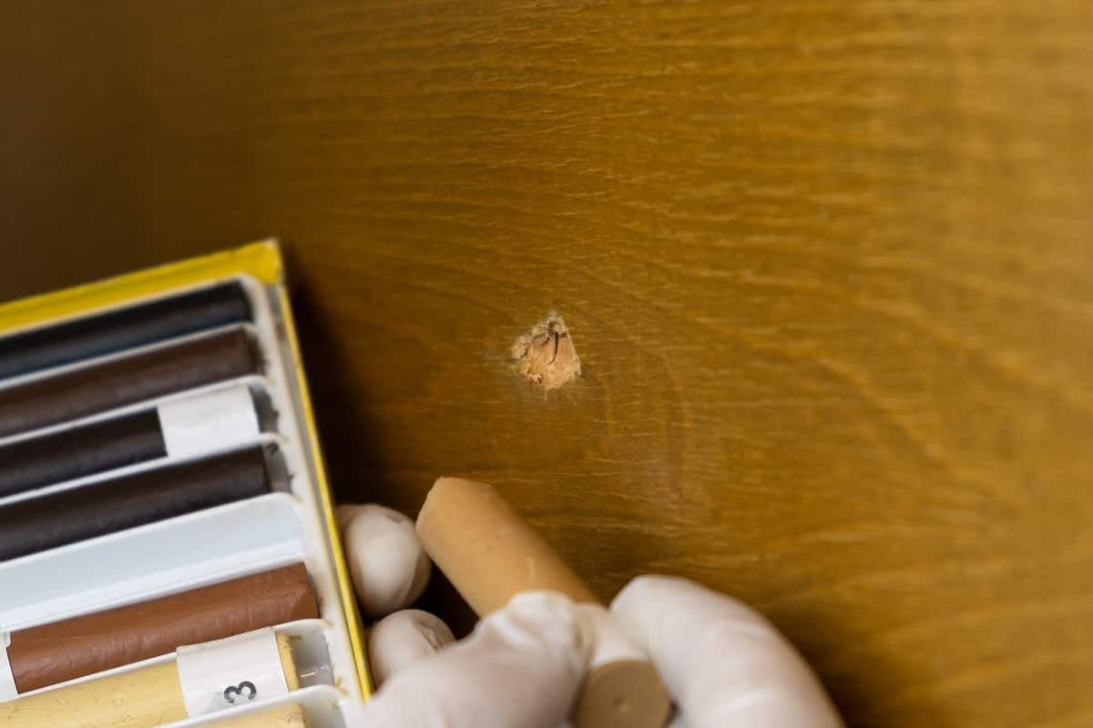 Furniture restoration,the master closes the hole in the wooden surface with wax pencils close-up.