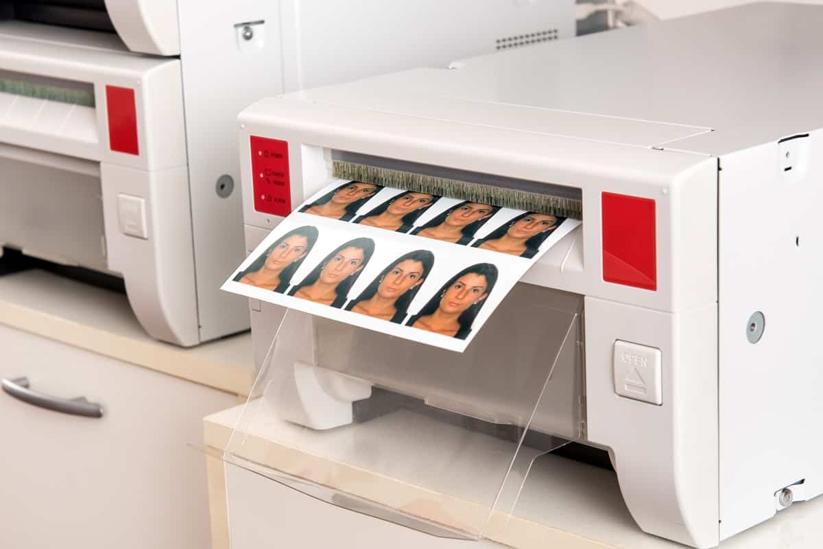Printing passport photos of a woman on a printer with a sheet of eight photographs exiting the machine in a close up view