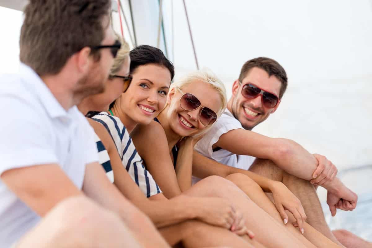 Vacation, travel, sea, friendship and people concept - smiling friends sitting on yacht deck