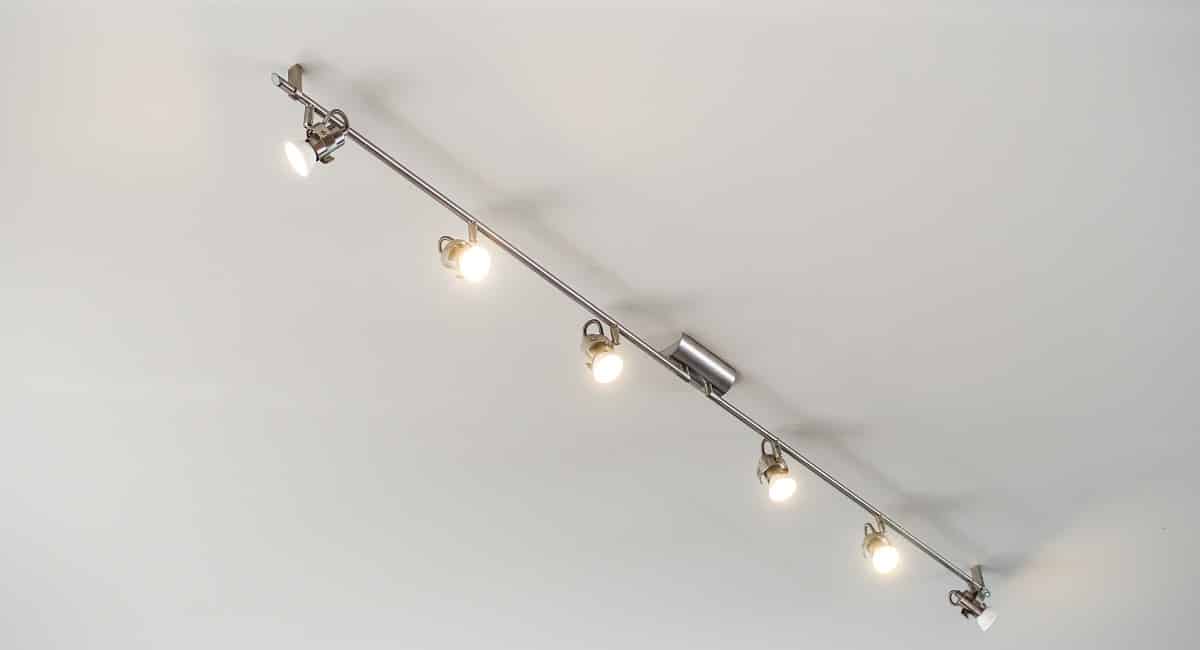 Modern stainless steel track light hanging on white ceiling background.. Track and rail lighting.