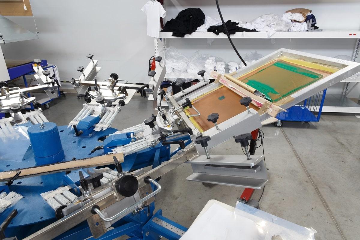 Screen printing machine for applying images by silkscreen printing. Print screening apparatus. Serigraphy production. Printing images on t-shirts in a design studio. Equipment for screen printing final thoughts.