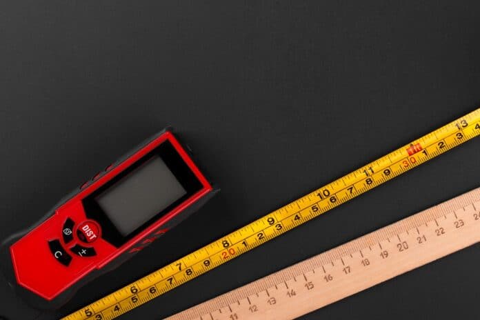 Fragment of tape measure, laser distance meter and outdated wooden ruler on dark matte surface. Flat lay. How Do Laser Measures Work.
