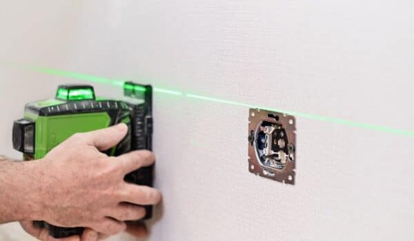 An electrician installs sockets in the apartment. Checking the installed sockets on the wall of the apartment with a laser level, selective focus on the sockets.