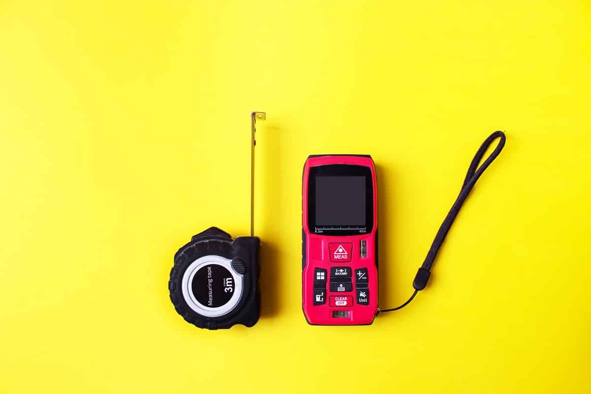 Laser rangefinder and measuring tape on yellow background. The measuring devices concept. Measuring tools for engineering frequently asked questions.